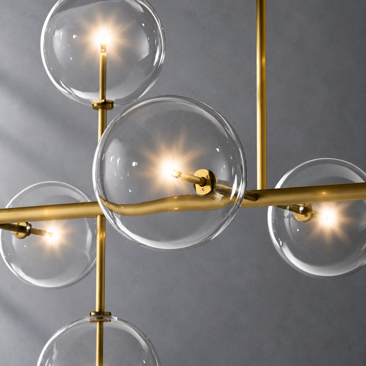 Sierra 72-inch lacquered burnished brass linear chandelier glass globe and metalwork detail on a textured gray background